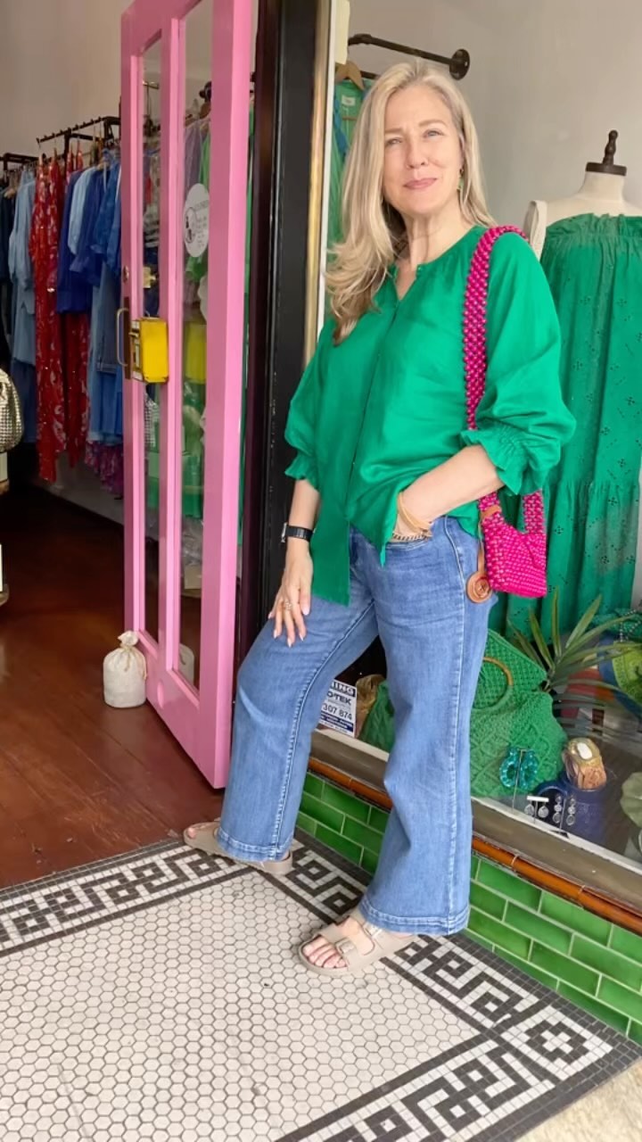Owner Jodi in a forest green blouse, straight light-blue jeans and an over-the-shoulder magenta pink bag. Jodi is standing outside her boutique located at 16 The Strand, Croydon, Sydney.
